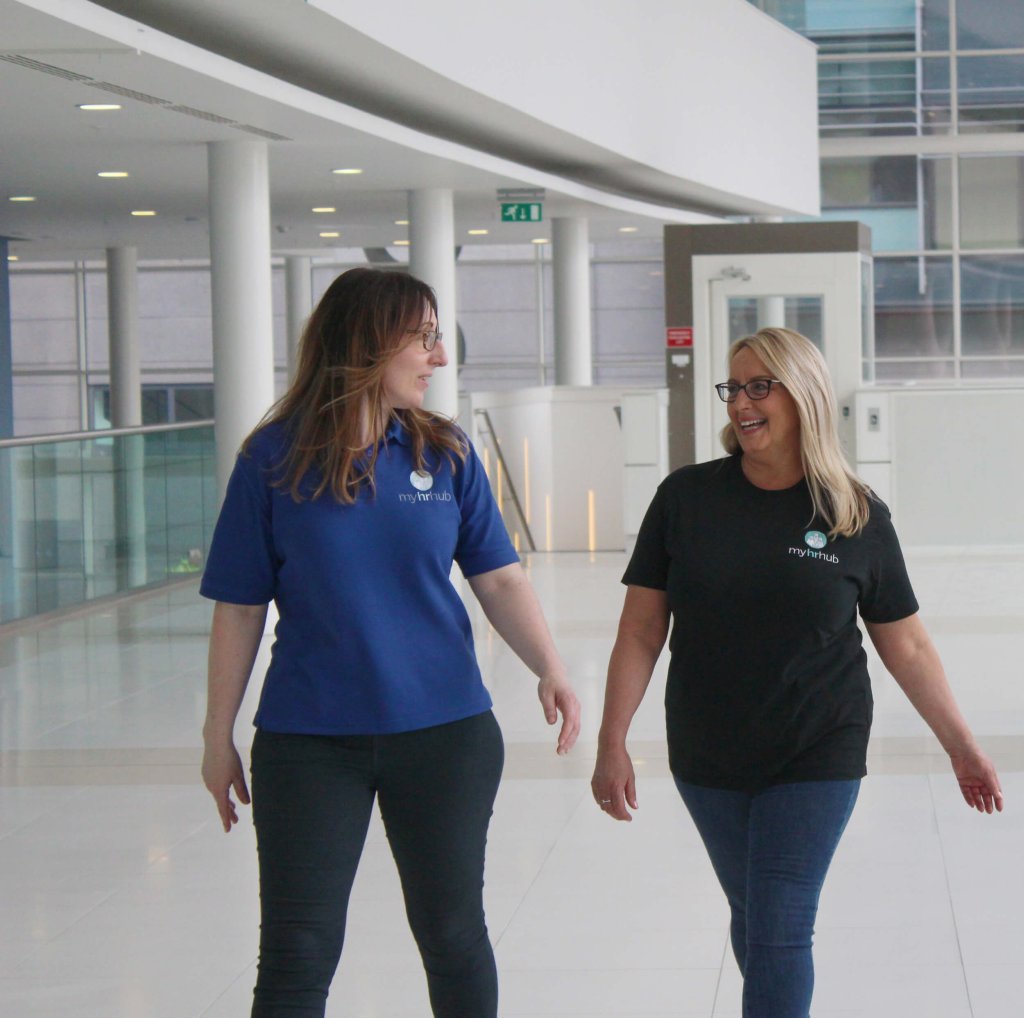 An HR team are walking through a corporate workspace. They are looking at each other an smiling.