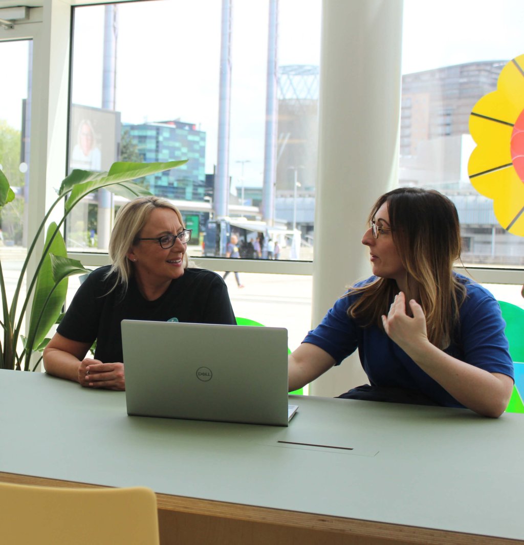 2 HR coaches are working on a shared laptop and talking to each other.