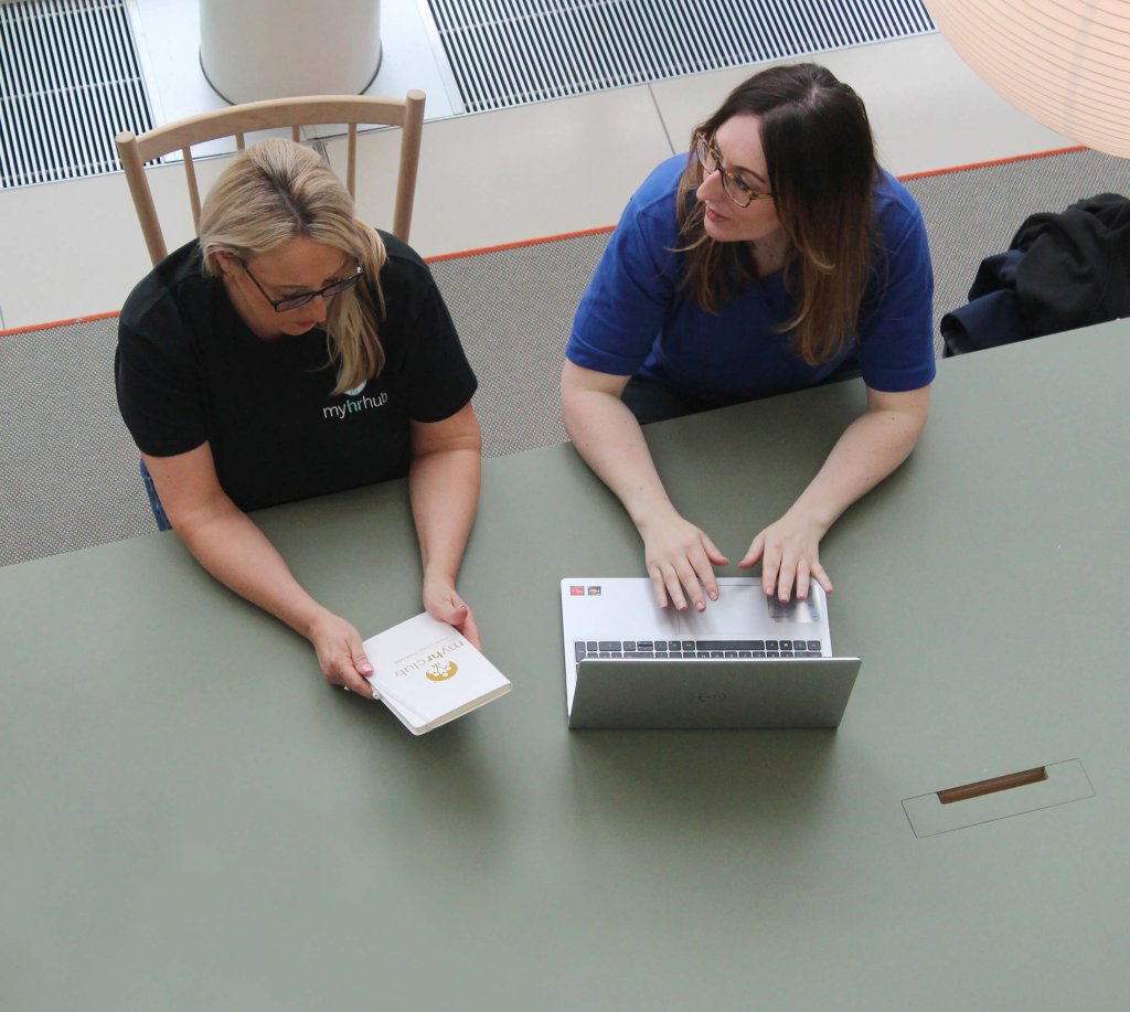 2 ladies are planning their HR services. They are both sitting at a table with a laptop and a booklet.